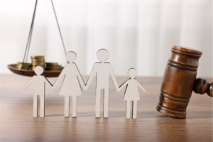 Figuras de papel representando familia de 4 pessoas, atrás martelo de juiz e moedas em balança - Execução de pensão alimentícia